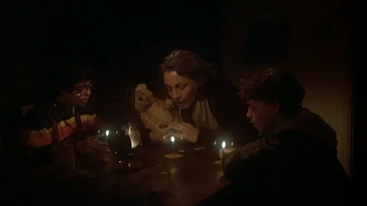 A woman and two boys pray around a candle-lit table.