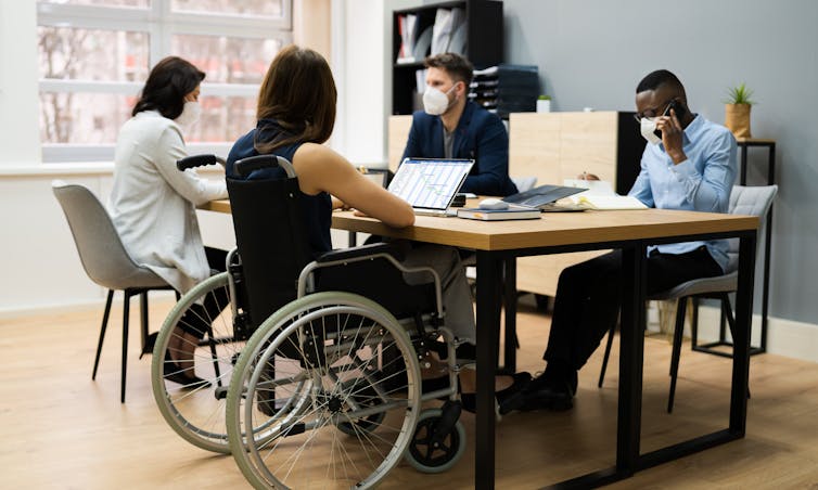 Students seen sitting at a work table, one in a wheelchair.