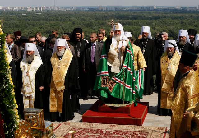 Archbishop Krill of the Russian Orthodox Church holding a cross in front of forests.