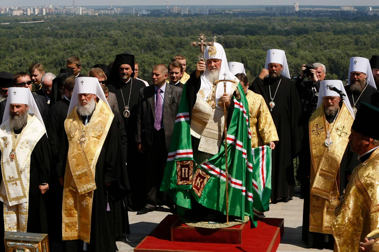 Archbishop Krill of the Russian Orthodox Church holding a cross in front of forests.