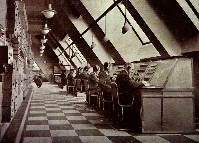 Black and white photo of men sat at desks in a control room.
