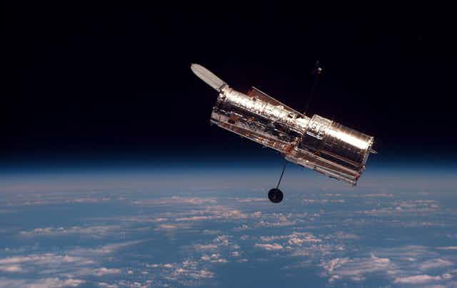 A shiny cylindrical telescope in orbit above Earth.