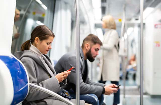 a woman and a man sitting on a train checking their phones