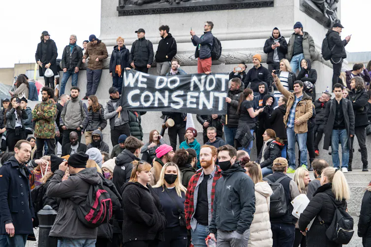 a group of people surrounding a banner reading WE DO NOT CONSENT