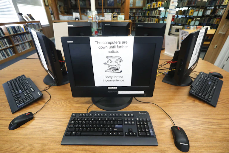 pieces of paper taped over computer monitors on a table in a room lined with bookshelves