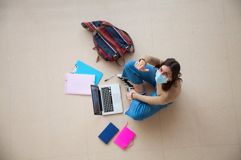 A student is seen sitting on the floor doing work giving a thumbs up.