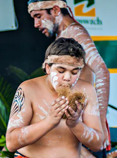 A young First Nations person stands in cultural paint, trying to ignite fire.