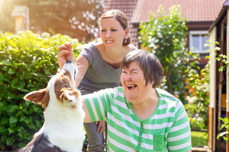 Carer and woman with disability playing with a dog.