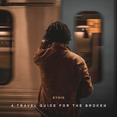 An album cover with a photo of a dreadlocked man in a brown coat from behind. In front of him a train passes.