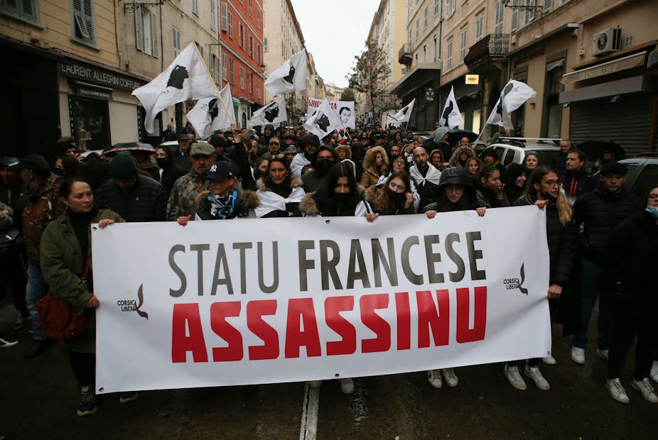 Des manifestants tiennent une banderole  "L'État français est un assassin", à Bastia, le 13 mars 2022, lors d'un rassemblement en hommage au militant indépendantiste Yvan Colonna, après son agression à la prison d'Arles. Ce dernier est décédé des suites de ses blessures le 21 mars 2022.
