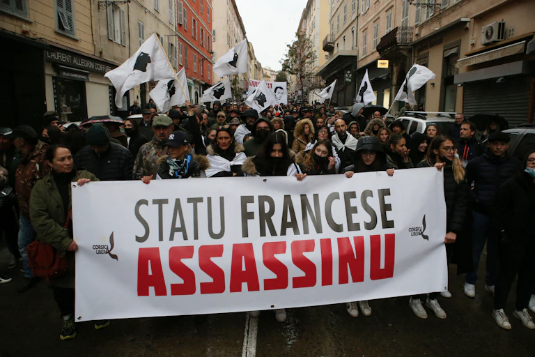 Des manifestants tiennent une banderole "L'État français est un assassin", à Bastia, le 13 mars 2022, lors d'un rassemblement en hommage au militant indépendantiste Yvan Colonna, après son agression à la prison d'Arles. Ce dernier est décédé des suites de ses blessures le 21 mars 2022.