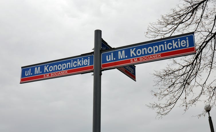 A set of red and blue street name signs seen against a cloudy class=