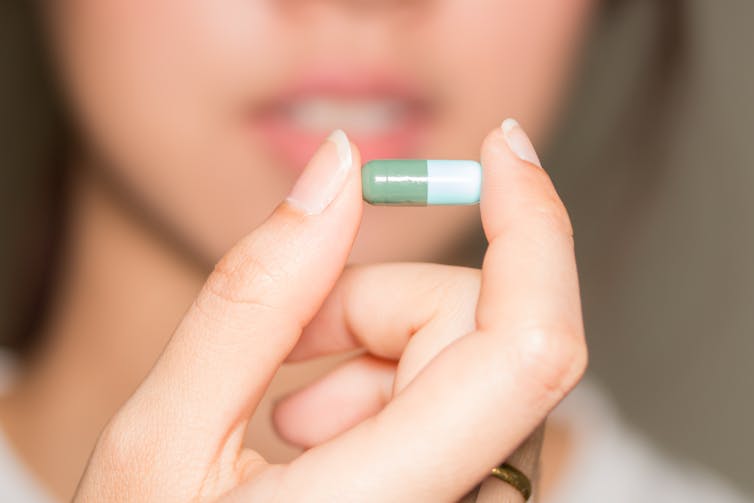 Woman holds an antibiotic pill between her thumb and index finger.
