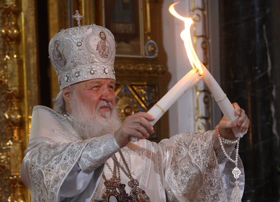 Russia's Patriach Kirill, wearing a white ceremonial dress holds up two large candles as he lights them.