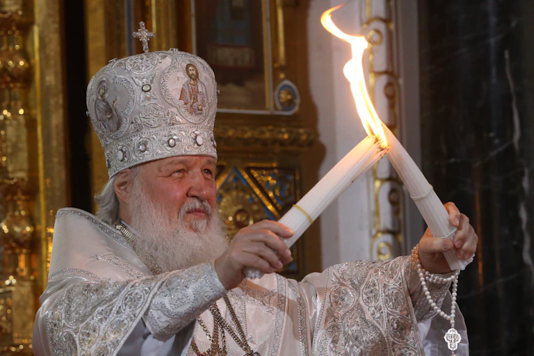 Russia's Patriach Kirill, wearing a white ceremonial dress holds up two large candles as he lights them.