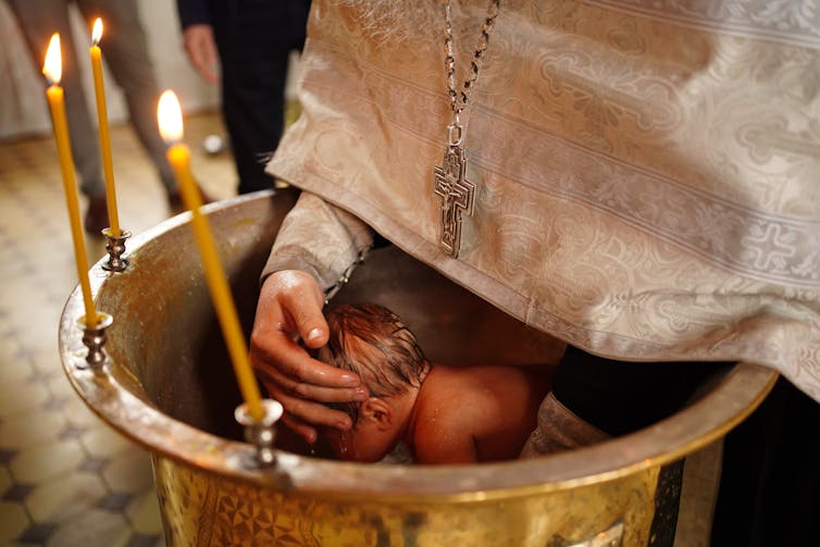 A priest holds a baby being lowered into the font for the baptism in the church.