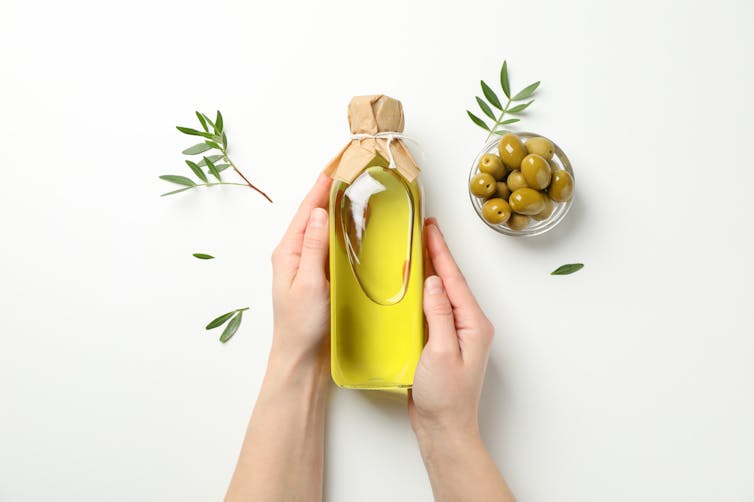 Dos manos cogen una botella de aceite de oliva.