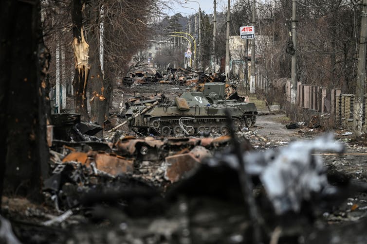 destroyed armored vehicles fill a tree-lined street