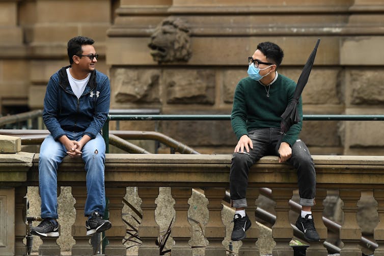 Two men sit outside Sydney Town Hall.