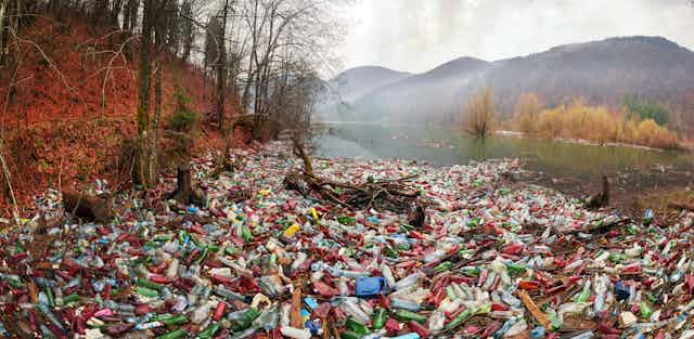 A pile of plastic waste near a water body with mountains in the background.