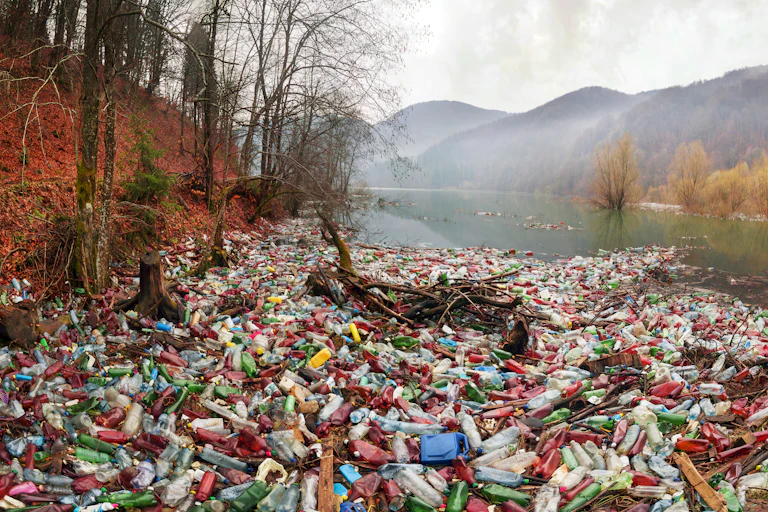 A pile of plastic waste near a water body with mountains in the background.