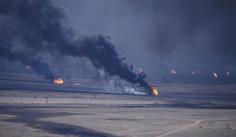 Oils wells burn and black smoke rises into the sky in a large oil field.