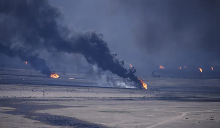 Oils wells burn and black smoke rises into the sky in a large oil field.