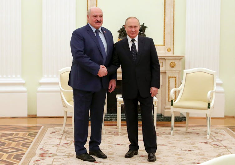 Two balding men in dark suits, one about six inches taller than the other, shake hands.