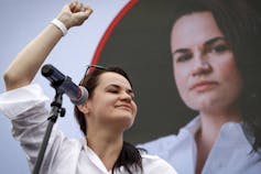 A dark-haired woman raises her fist. A large photo of her face is behind her.