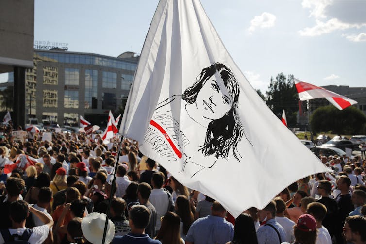 Protesters gather carrying a flag with a woman's face on it.
