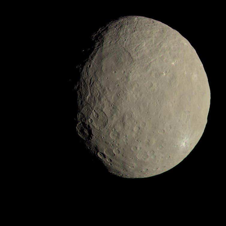A photo of the dwarf planet Ceres.  To the human eye it appears a sandy brown color and is pockmarked with craters.