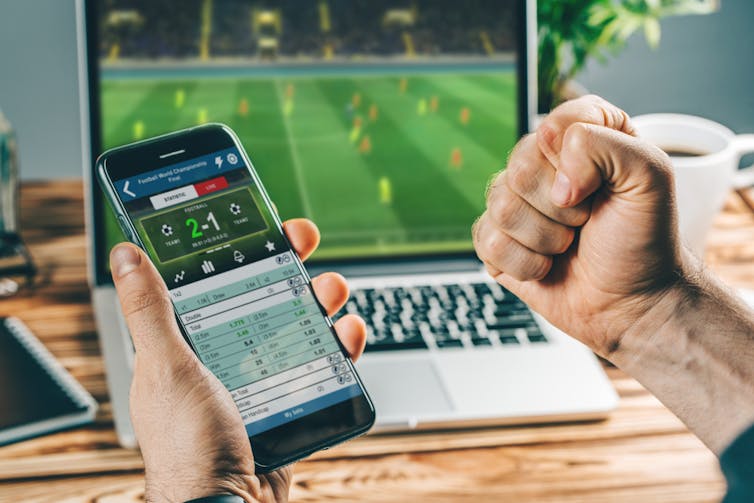 Hand holding a phone while sports betting, the other fist clenched in celebration