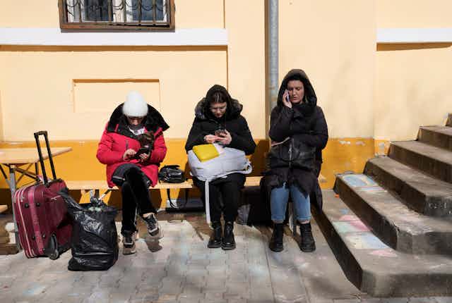 three women on their mobile phones sit outside a building