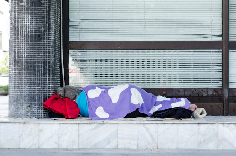 A homeless person sleeping under a blanket outside a building