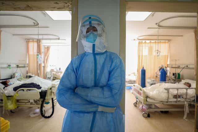 nurse in protective clothing leans against a wall in a hospital