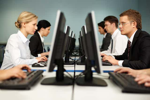 two rows of people facing each other working on desktops