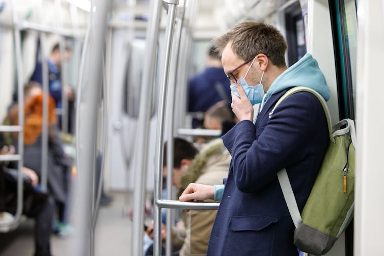 Man on train coughs into his mask