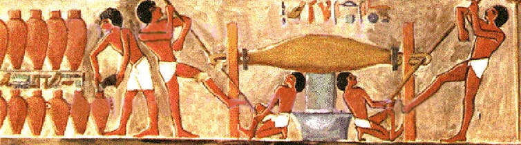 A colourful Egyptian wall painting depicting two men twisting a bag to produce a liquid and another man filling clay jars with liquid
