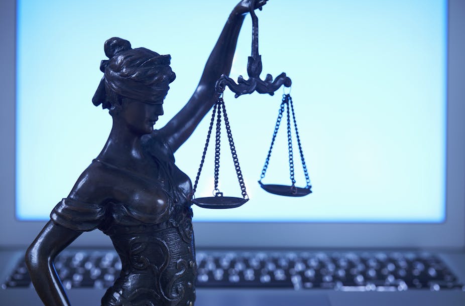 A small statue of Lady Justice holding scales stands in front of a blank laptop screen.