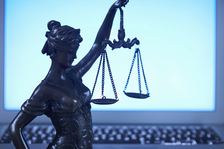 A small statue of Lady Justice holding scales stands in front of a blank laptop screen.