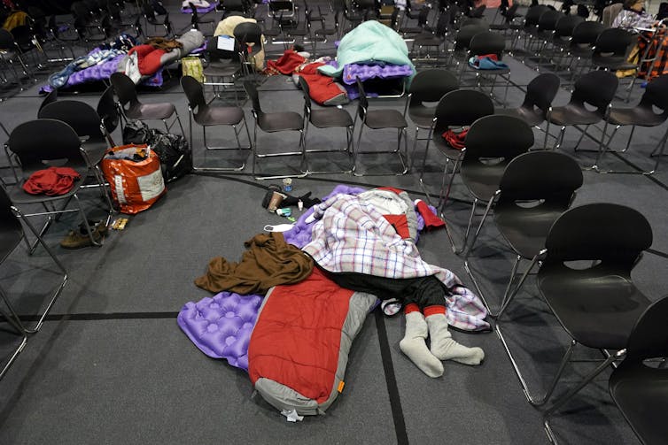 A person lies on the floor of a large meeting room, covered with fleece blankets