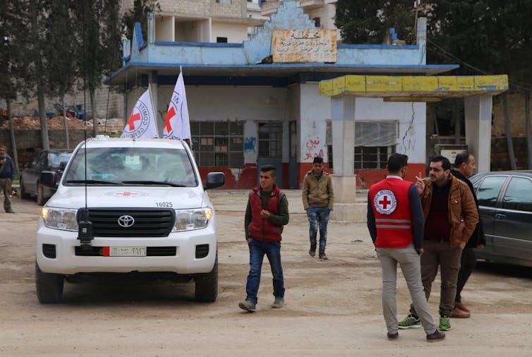 Men in International Committee of the Red Cross vests speak with locals in a Syrian village.