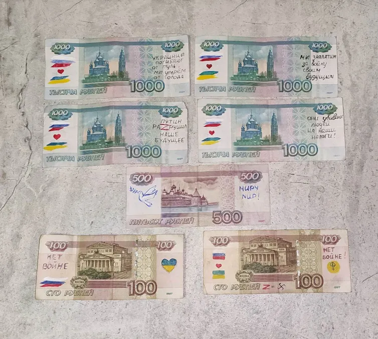 Rows of Russian bank notes (paper money) seen laid out on a table showing hand-written messages.