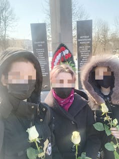 Trois femmes vêtues de noir et portant des roses blanches sont vues ensemble, les visages étant floutés pour des raisons de confidentialité