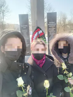 Three women wearing black carrying white roses are seen standing together with faces blurred out for privacy.