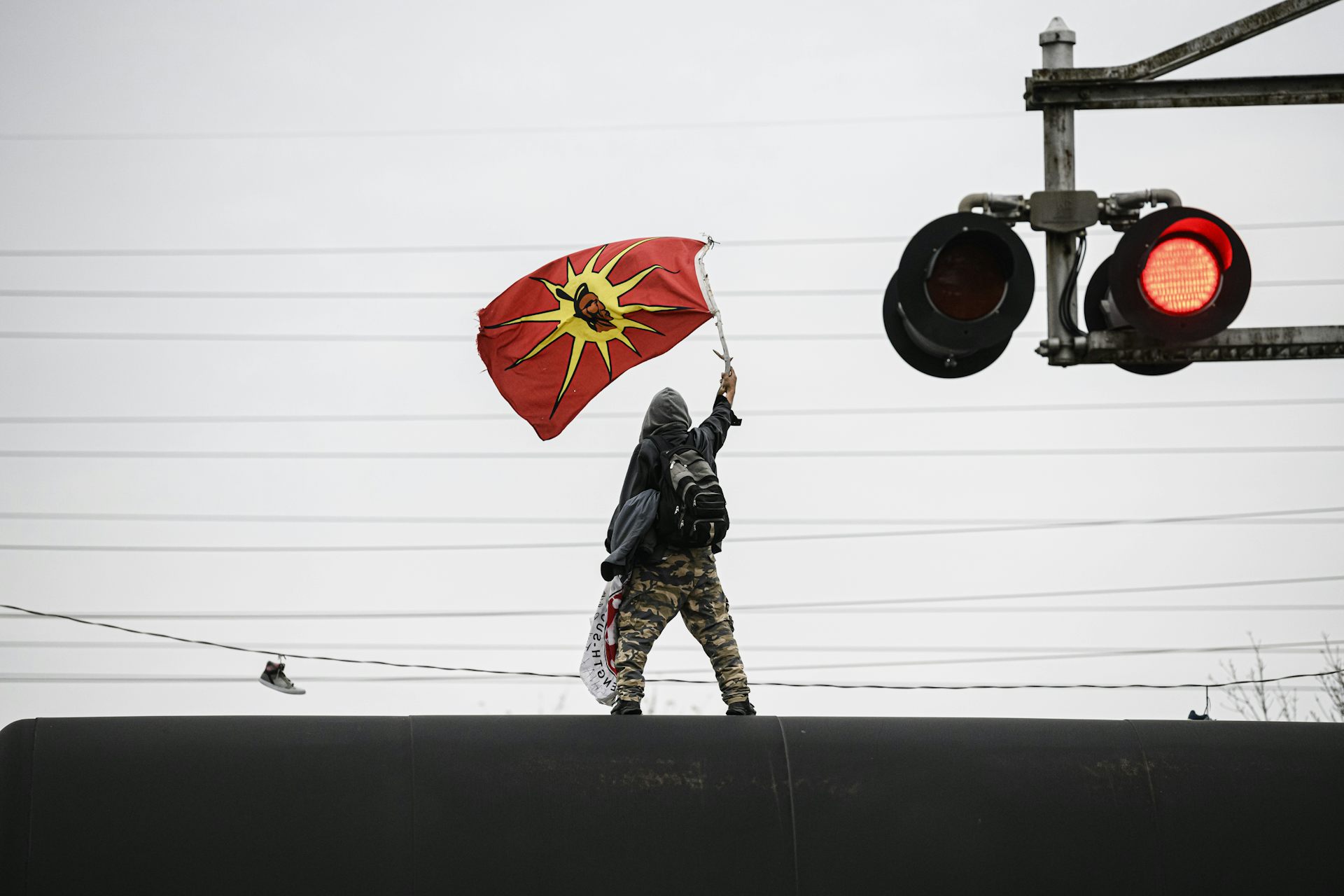 A man waves an orange and yellow flag while standing on a rail line.