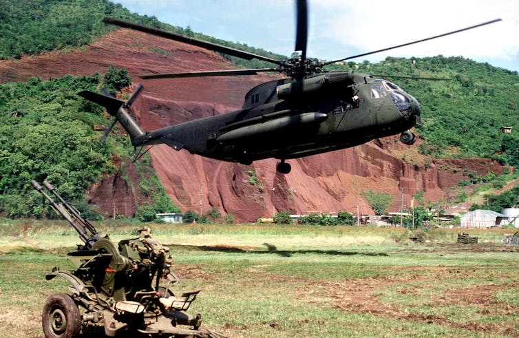 A helicopter hovers above an anti-aircraft weapon.