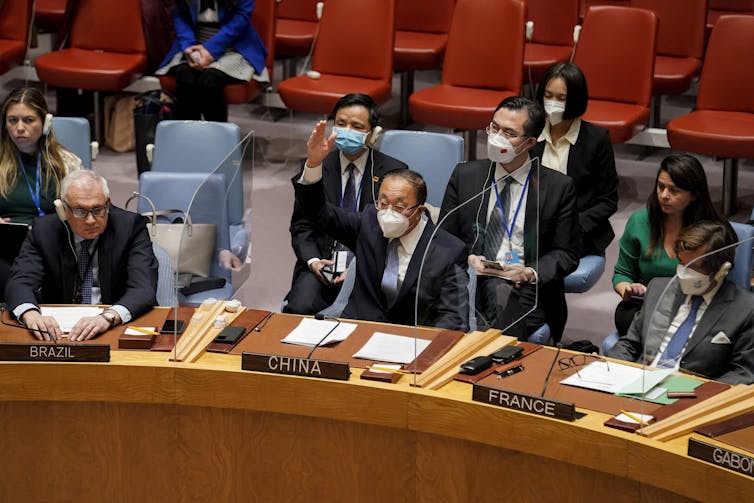 diplomats in business suits and surgical masks seated in a hall