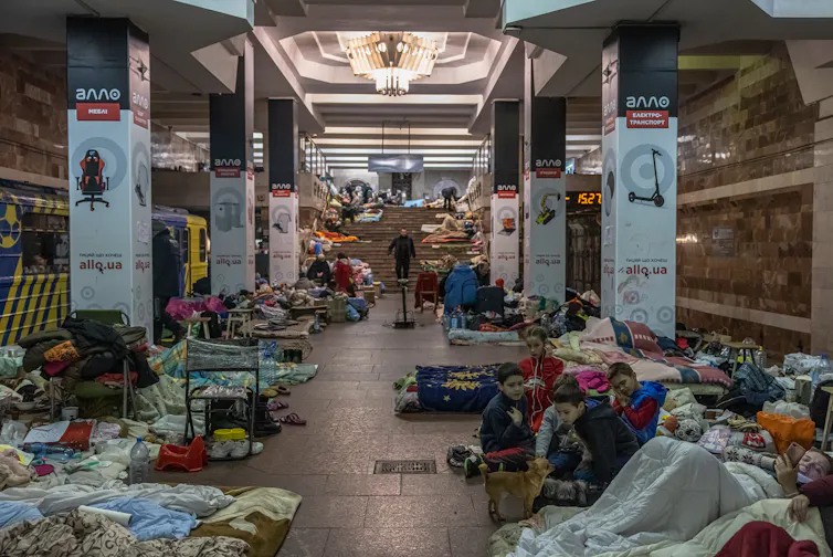Ukrainian adults and children line a subway platform to take shelter from bombs, along with many of their belongings.