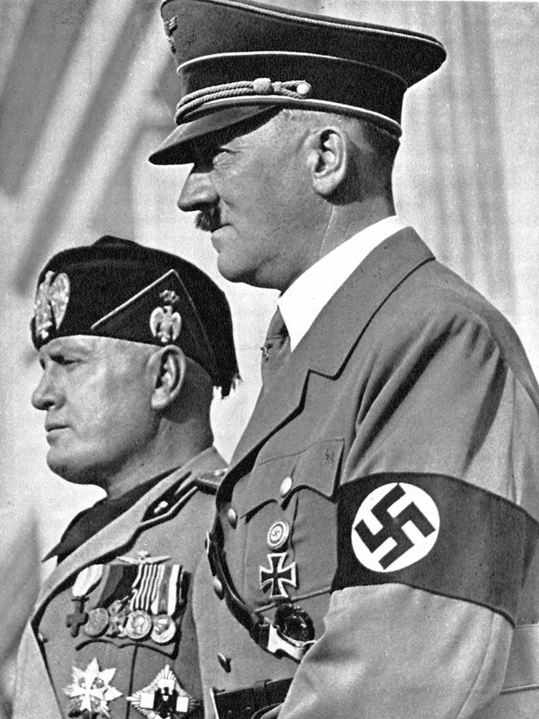 Two men in military uniform with medals on their chest.  A man wears a Nazi swastika armband.